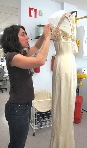 Une restauratrice procède aux derniers ajustements d'une robe sur un mannequin, après la restauration.
